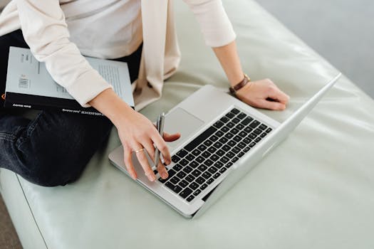 An adult using a laptop for remote work, multitasking with a book.