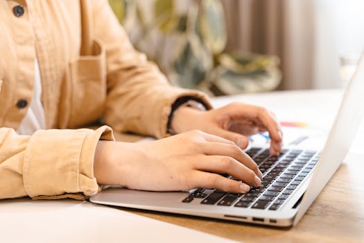 Close-up of hands typing on a laptop in a bright indoor setting, emphasizing work and technology.