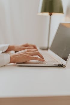 Close-up of hands typing on a laptop in a bright minimalistic office setting.