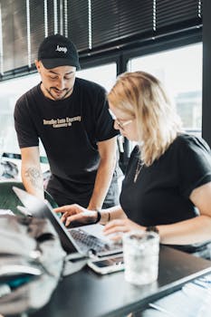 Two colleagues work together on a laptop in a bright, modern office setting, showcasing teamwork and productivity.