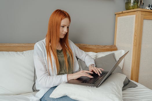 Red-haired woman focused on laptop work from home setting.