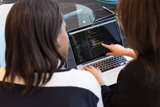 Two women working together on software programming indoors, focusing on code.