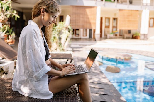 Woman with curly hair working on a laptop by the pool in Bali, Indonesia.